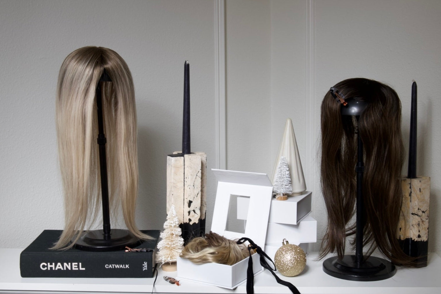 Two mannequin heads with wigs on a white surface against a gray wall.